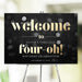 Personalized Four-Oh 40th birthday welcome sign with custom name, black bokeh background, warm gold lettering and celebration date
