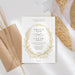White wedding invitation with a gold floral wreath, botanical leaves, ribbon bow and personalized ceremony details-front