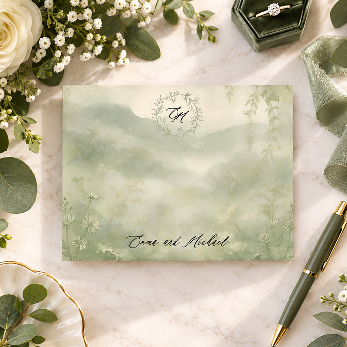 Personalized wedding note card with leafy monogram wreath, Emma and Michael names, misty sage watercolor landscape and delicate wildflowers-front