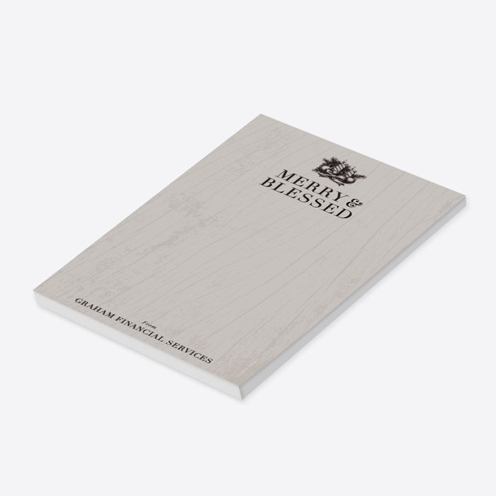 Personalized holiday notepad featuring “Merry and Blessed” text with wood grain, pine boughs, ornaments, ribbon, and candle illustrations. -side