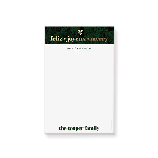 personalized holiday notepad with evergreen border, Feliz Joyeux Merry wording, custom family name, and blank writing space