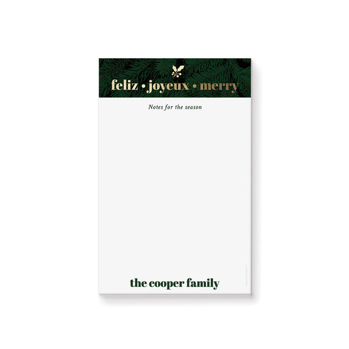 personalized holiday notepad with evergreen border, Feliz Joyeux Merry wording, custom family name, and blank writing space