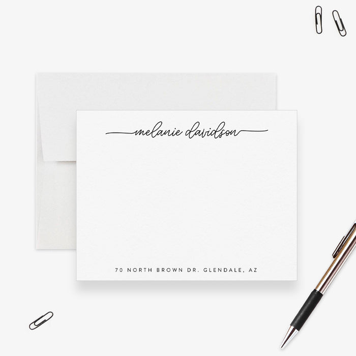 Black and white personalized note card with script name and address line, shown with a white envelope and pen-front