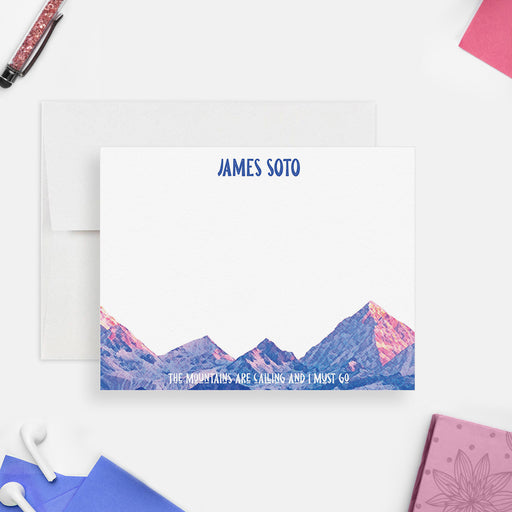 Personalized mountain note card with a blue name, pink and blue peaks and “The mountains are calling and I must go” beneath the white writing area.