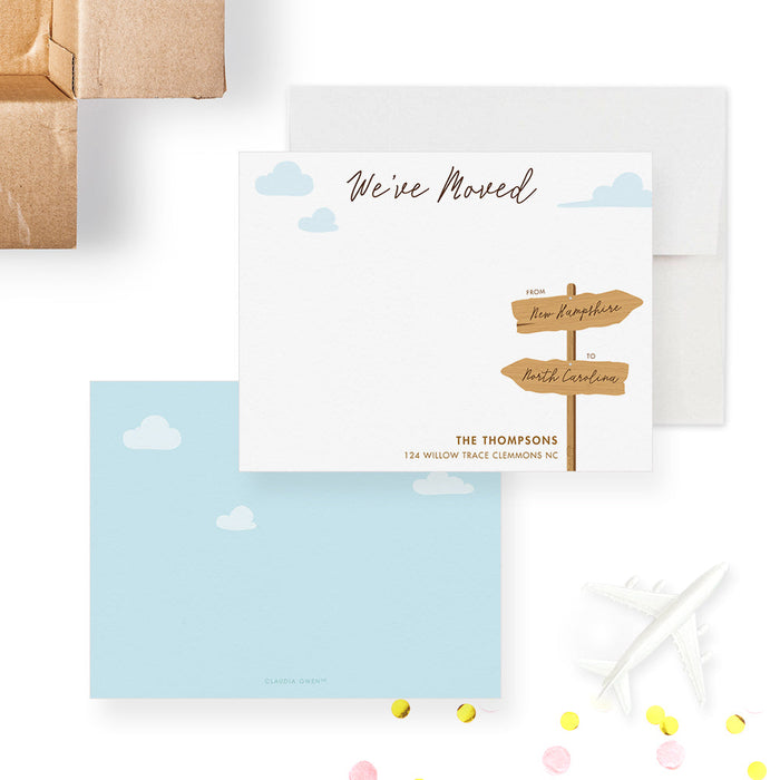 Front and back of personalized note cards with a wooden moving sign, blue sky, clouds and personalized new address details and a blue sky and cloud patterned back.