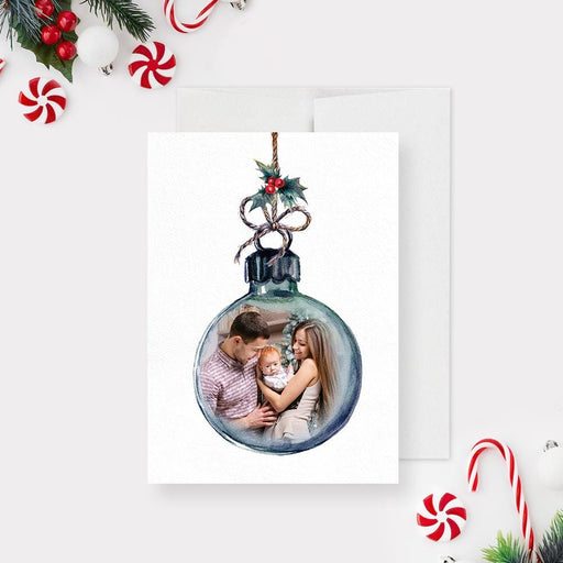 Watercolor Christmas ornament photo card featuring a round bauble frame with a family portrait inside, decorated with holly and a twine bow