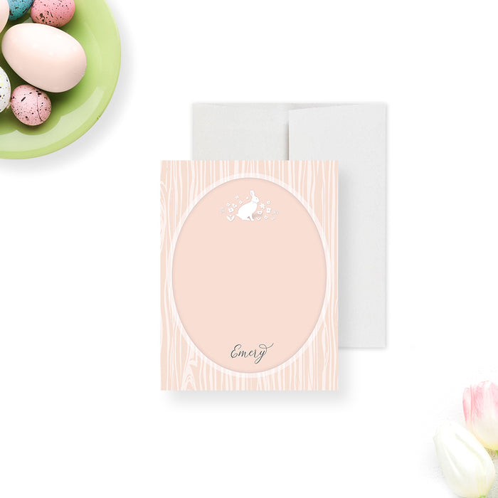 Personalized note card with a pink patterned front with an oval writing area, a floral bunny illustration, and a name. Shown with a white envelope.