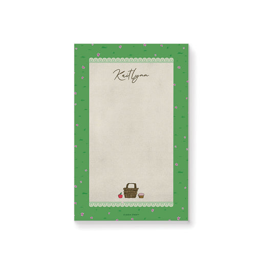 personalized spring picnic notepad with custom name, picnic basket illustration, lace border, green grass pattern, and tiny pink flowers