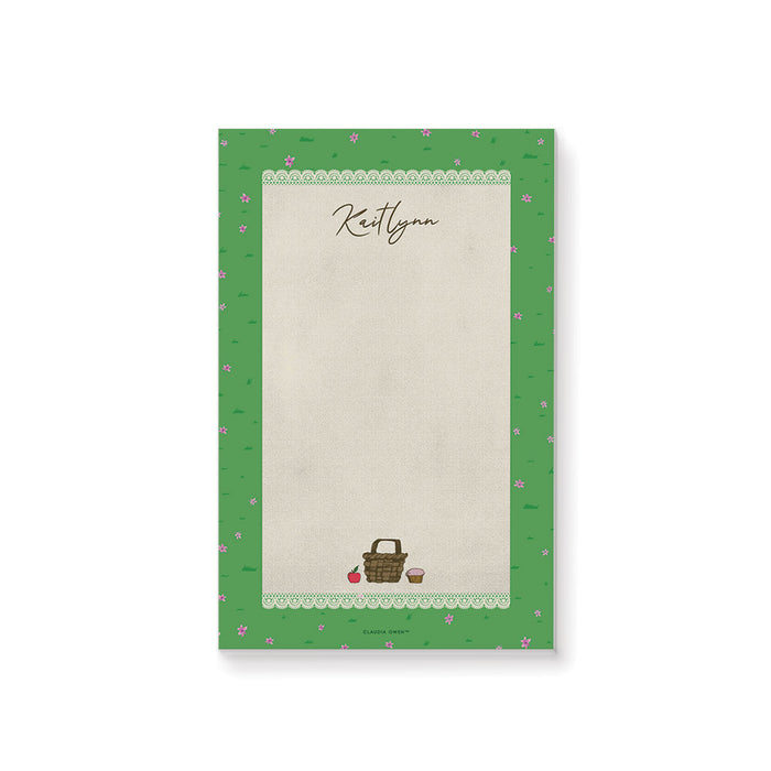 personalized spring picnic notepad with custom name, picnic basket illustration, lace border, green grass pattern, and tiny pink flowers