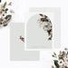 Front and back of personalized note cards with white flowers and greenery around an arch design with personalized names and a pale green back with a white floral illustration.