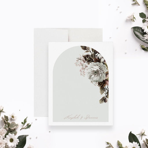 Personalized note card with white flowers and greenery around an arch design with personalized names, shown with a white envelope.