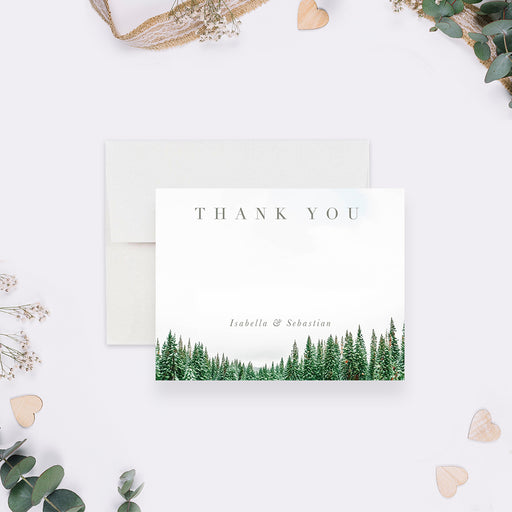 White personalized wedding thank you note card with snow-dusted green pine trees along the bottom, beside a matching forest back.
