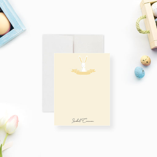 Personalized note card with a soft yellow front with a white bunny illustration and a name in script. Shown with a white envelope.