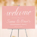 Romantic pink engagement party welcome sign with elegant script lettering displayed on an easel for a wedding celebration