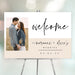 Modern wedding welcome sign featuring the couple's photo, their names, and wedding date in elegant script and neutral tones.