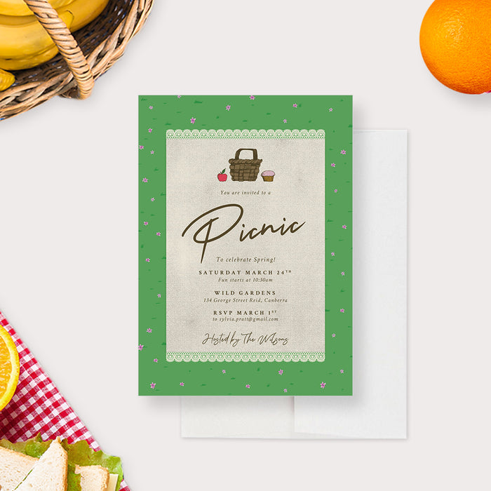 spring picnic invitation with picnic basket illustration, green garden border, lace-style detail, and small floral accents for an outdoor garden party