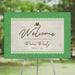 spring picnic party welcome sign with picnic basket illustration, lace border, green grass pattern, tiny pink flowers, and elegant script lettering