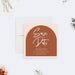 housewarming save the date card with terracotta arch design, blush border, white lettering, and custom new home party details-front