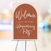 housewarming welcome sign with a terracotta arch on a blush pink background and elegant script lettering