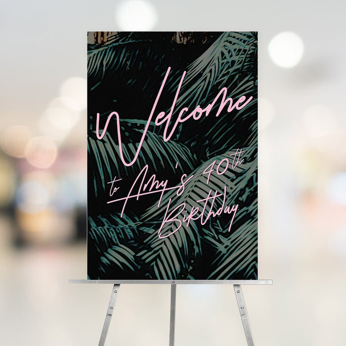 tropical birthday welcome sign with dark green palm leaves, pink welcome lettering, and personalized birthday text displayed on an easel