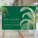 tropical wedding welcome sign with gold palm tree illustrations on an emerald green background for destination weddings and beach ceremonies