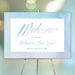Valentine's Day welcome sign with soft blue watercolor border, elegant script lettering, and personalized lunch details displayed on an easel
