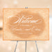 Vintage peach wedding welcome sign with white floral lace borders, elegant script lettering, and personalized couple names.
