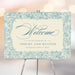 Blue botanical wedding welcome sign with vintage floral border and ivory background displayed on easel
