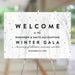 Elegant winter gala welcome sign with snowy forest background and gold confetti accents, displayed on an easel – customizable with event details.