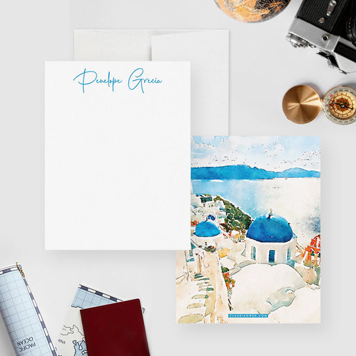 Santorini note cards with a blue script name on the white front and a watercolor scene of blue domes, white buildings and sea on the back.